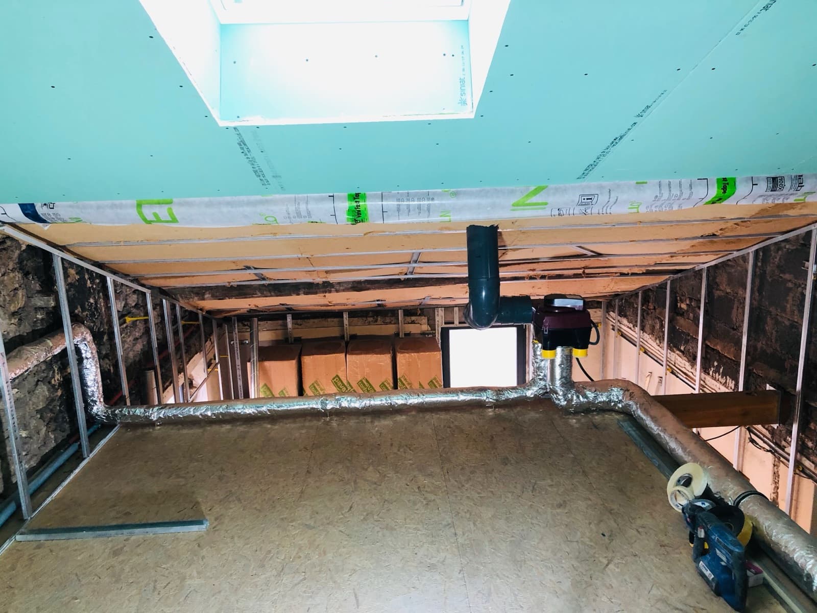 Réseau de gaines isolées et caisson VMC en cours de pose sous charpente